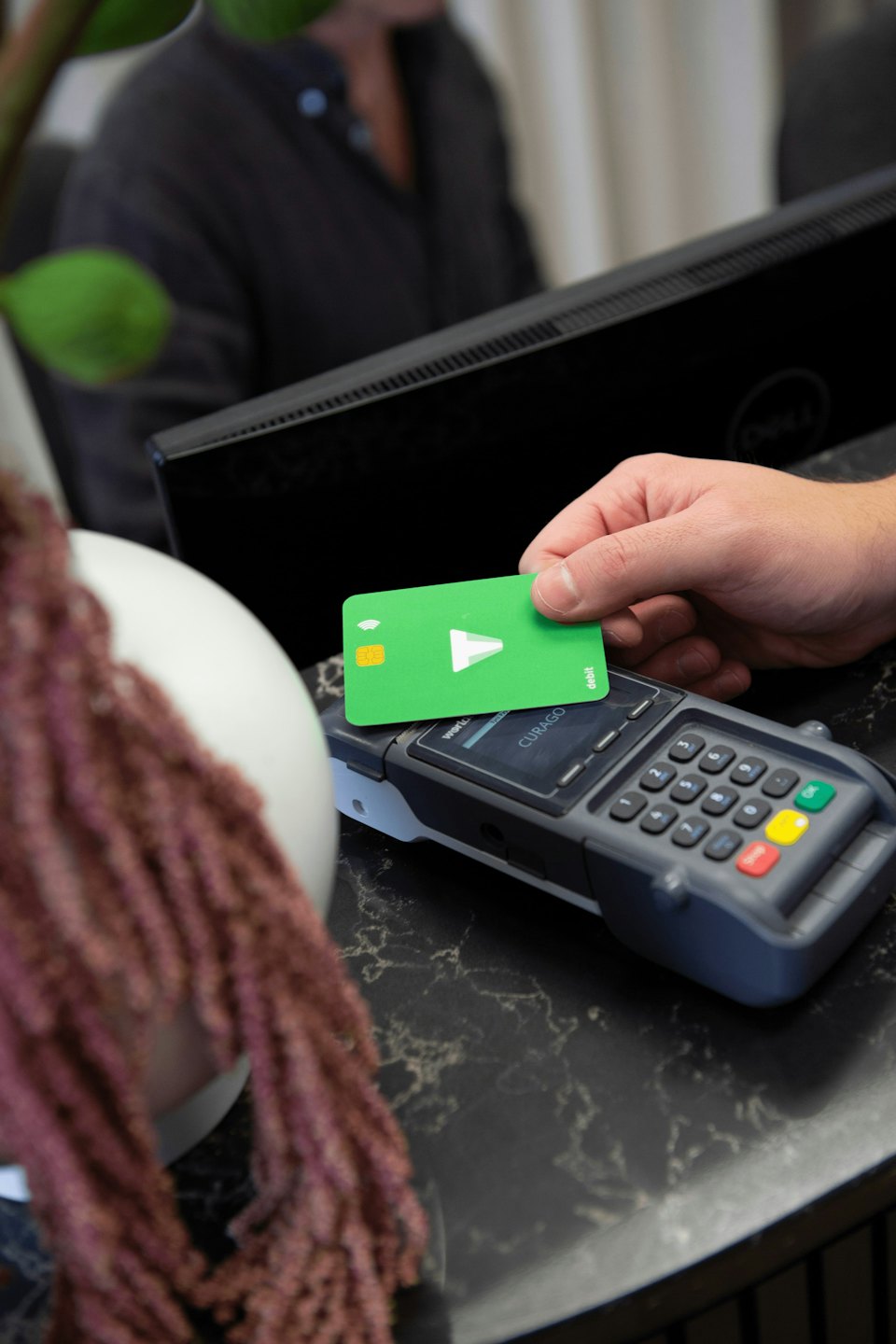 A hand holding a green card over a payment terminal.