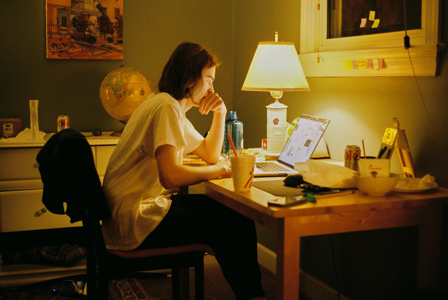 Person concentrating on a laptop at a cluttered desk.